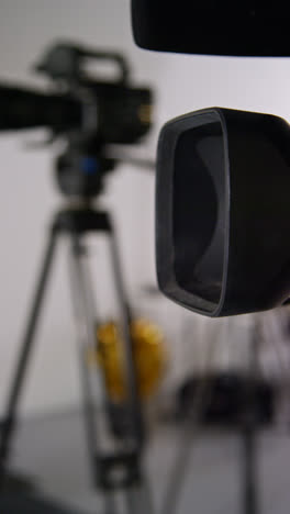 Vertical-Video-Close-Up-Of-Film-Camera-With-Lens-Hood-On-Tripod-Shooting-Movie-In-Studio